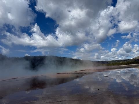Steam drifting across a thermal pool that mirrors the clouds