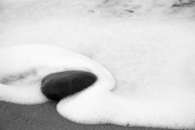 A dark stone wrapped in a curve of white sea foam — black and white