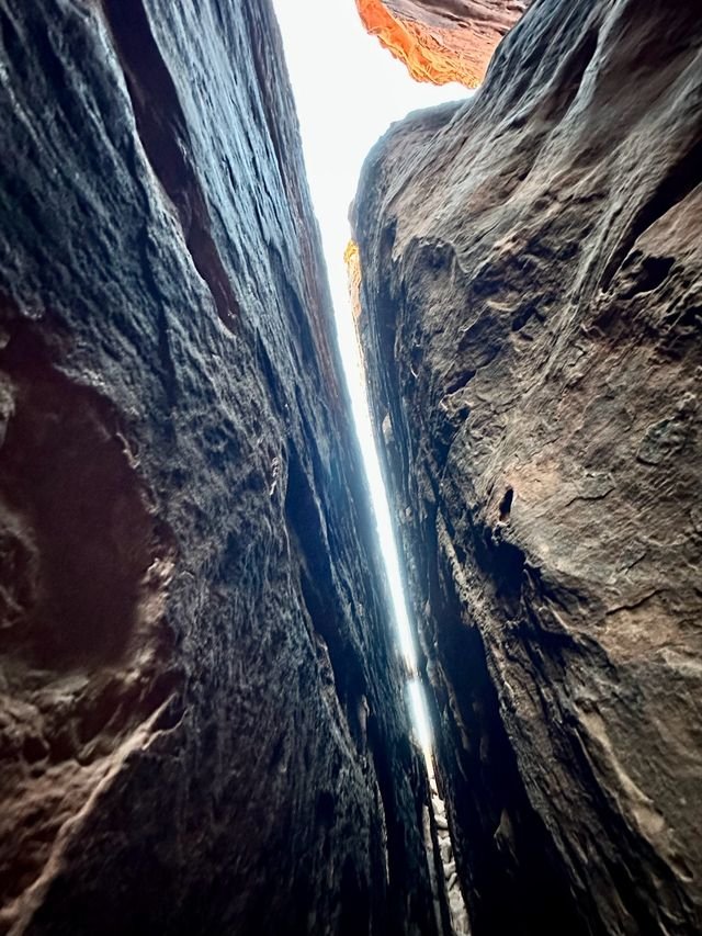 A sliver of light through a slot canyon, orange rock glowing overhead